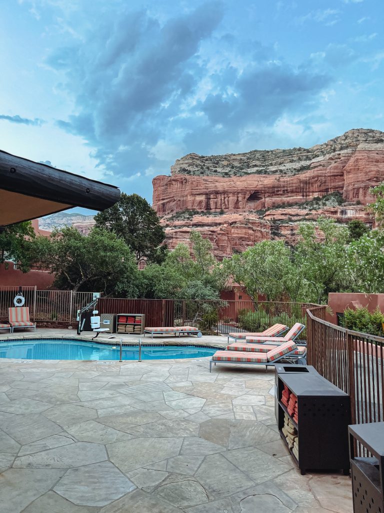 a pool with chairs and a fence in front of a red rock mountain
