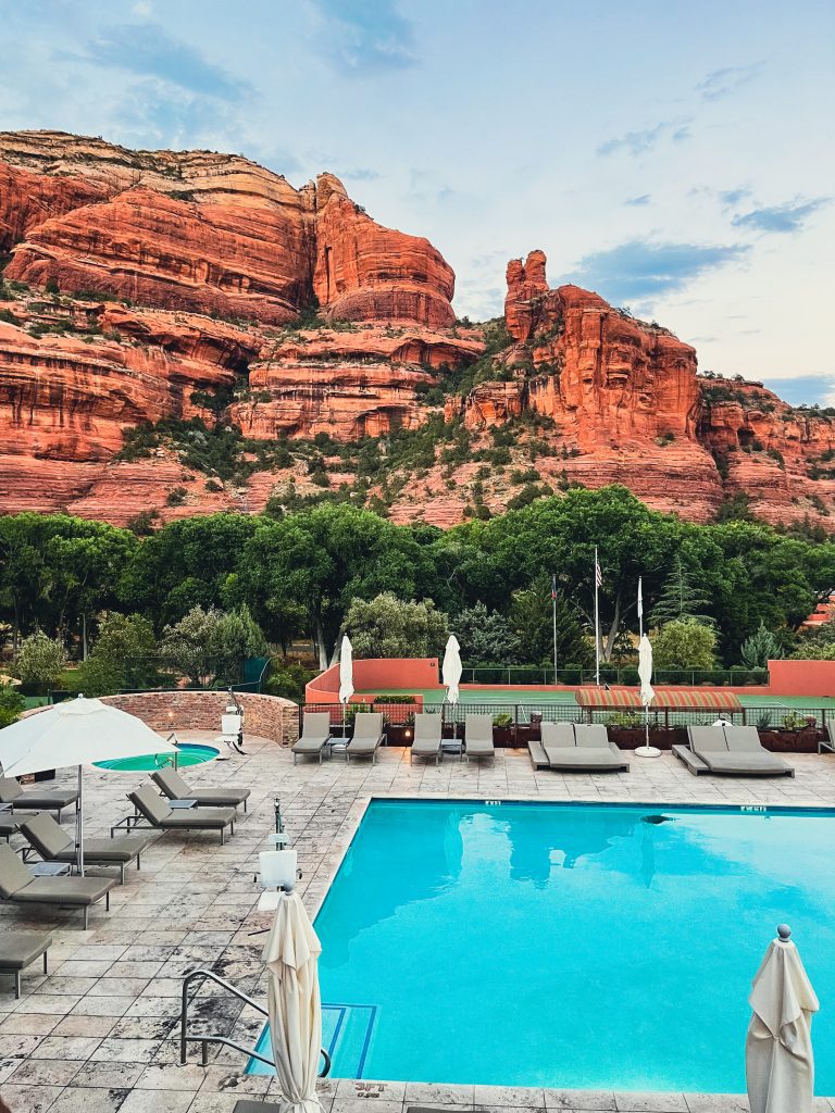 a pool with chairs and umbrellas in front of a red rock mountain