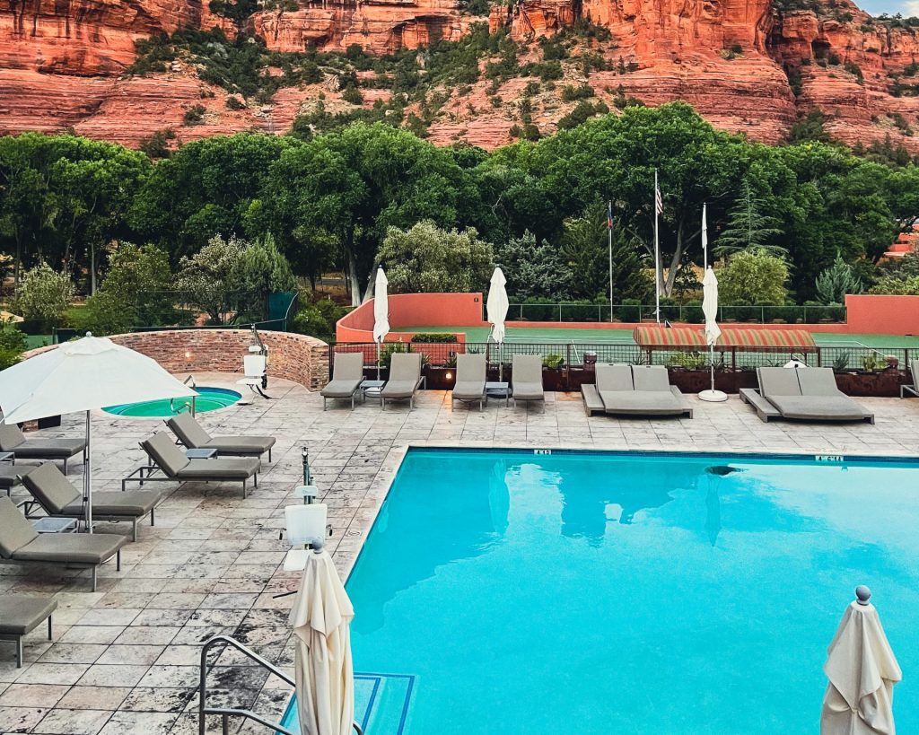 a pool with chairs and umbrellas in front of a red rock mountain