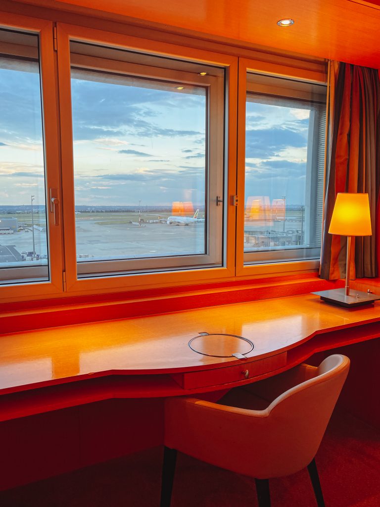 a desk with a lamp and a window with a view of an airport