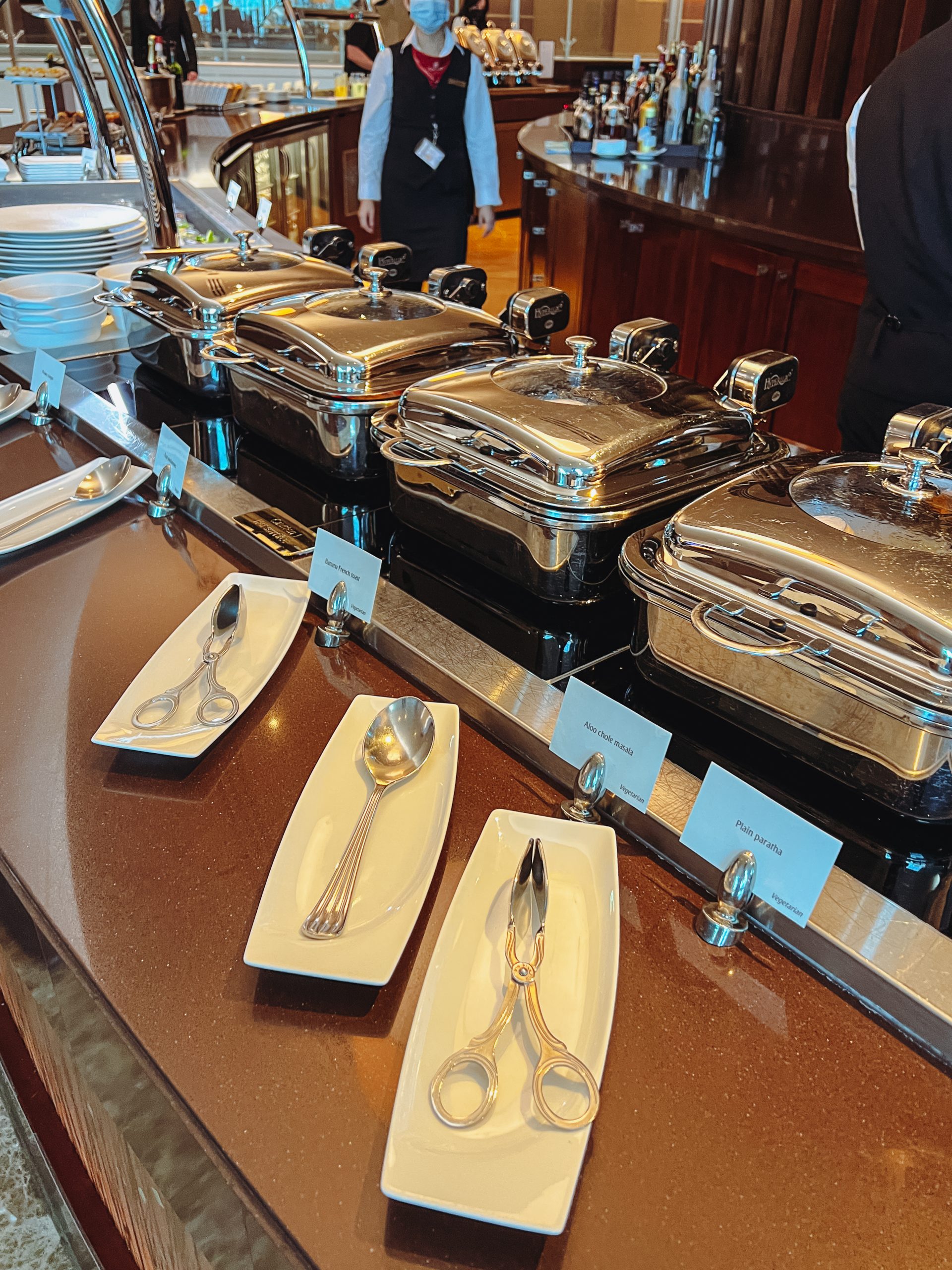 a buffet line of silver containers with silverware on a counter