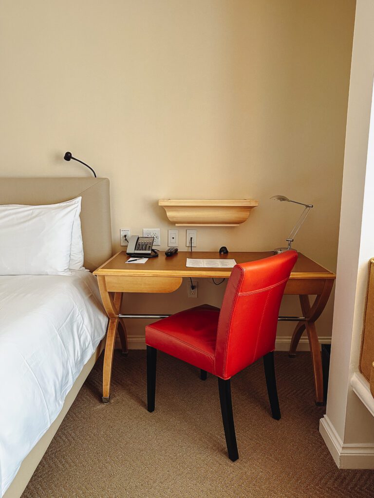 a desk with a red chair and a lamp in a hotel room