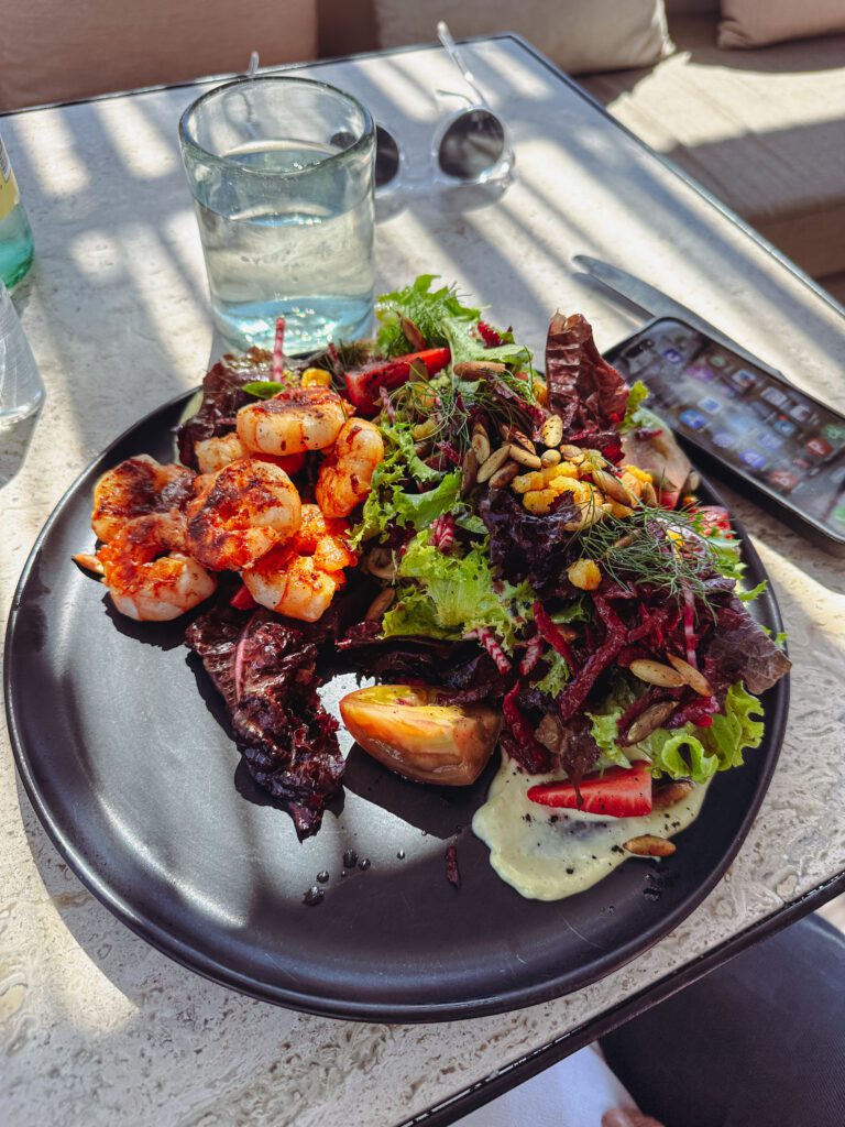 a plate of salad with shrimp and a phone on a table